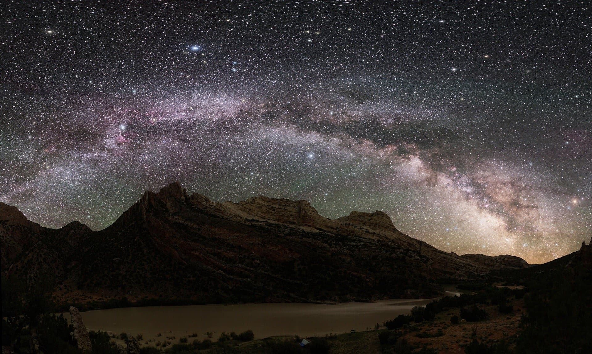The Milky Way arching over a dark mountain range and a still lake